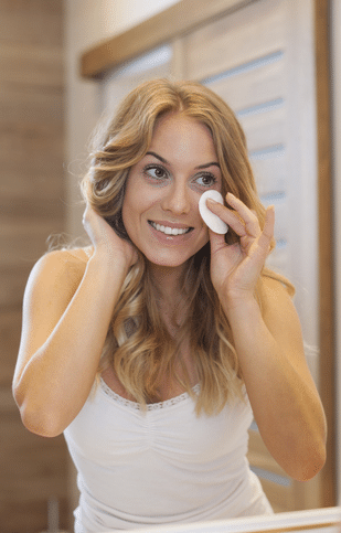Blonde woman cleaning face in front of mirror | Light Therapy